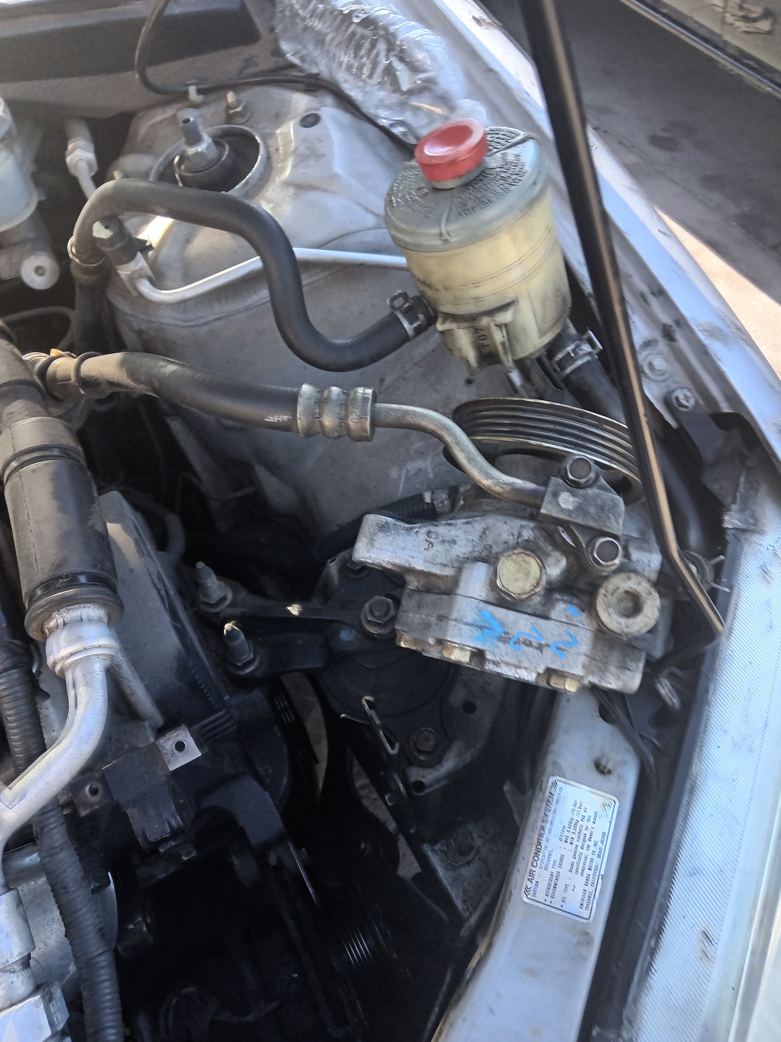 Engine bay showing power steering reservoir, AC compressor and hoses
