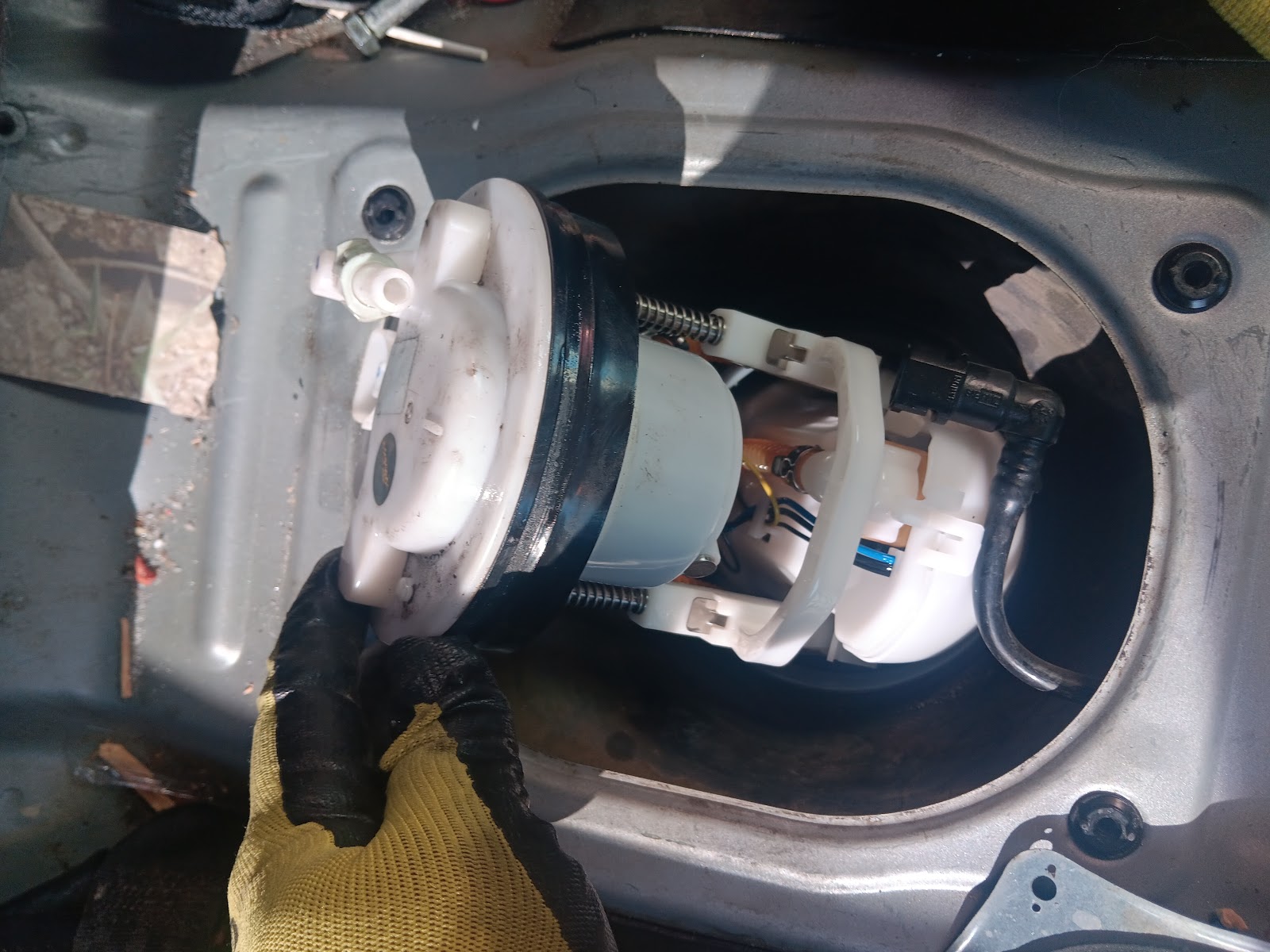Gloved hand removing fuel pump assembly from a fuel tank